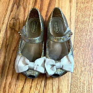 Mini Melissa hold hello shoes with bows.